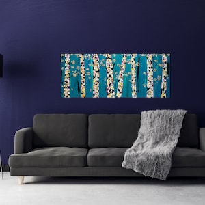 May include: A teal and yellow abstract painting of trees with white accents hangs above a gray couch with a gray throw blanket.