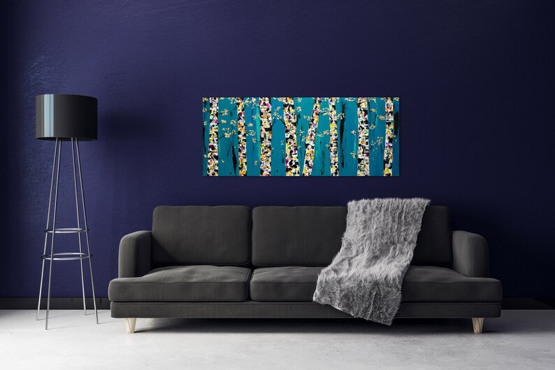 May include: A teal and yellow abstract painting of trees with white accents hangs above a gray couch with a gray throw blanket.