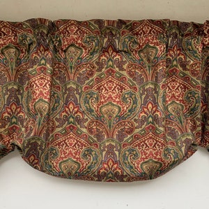 May include: A valance with a repeating paisley pattern in shades of red, green, and gold. The fabric is gathered at the top, creating a scalloped effect along the bottom edge. The valance is designed to be hung above a window.