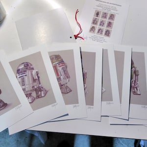 Puede incluir: Una colección de nueve impresiones enmarcadas con ilustraciones de personajes de Star Wars, incluyendo R2-D2 y C-3PO. Las impresiones son todas en blanco y negro y tienen un estilo vintage.