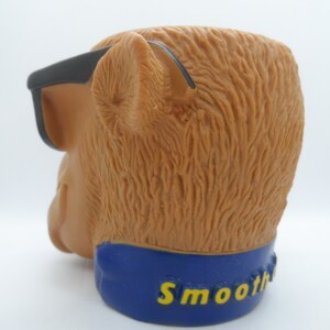 May include: A brown plastic monkey head with black sunglasses and a blue band around the bottom that says "Smoothie".
