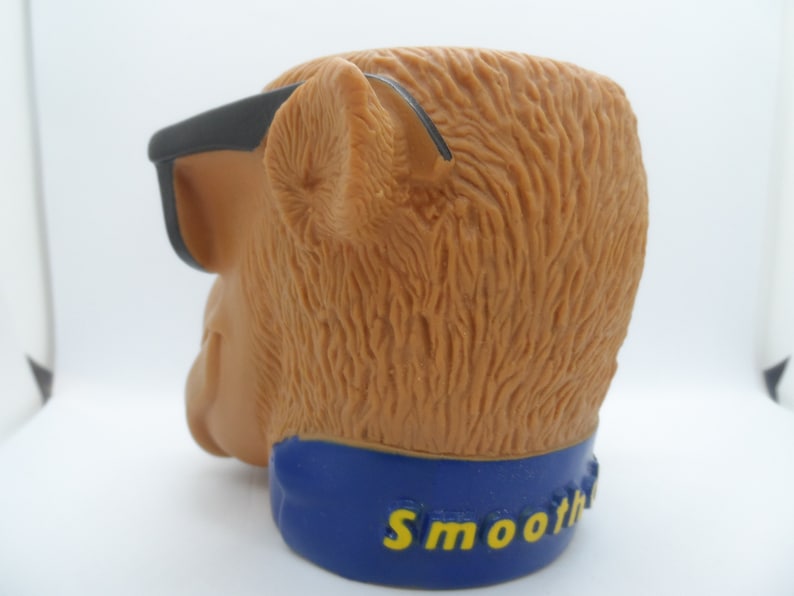 May include: A brown plastic monkey head with black sunglasses and a blue band around the bottom that says "Smoothie".