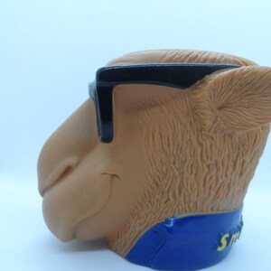 May include: A brown camel head figurine wearing black sunglasses and a blue and yellow collar with the word "Smokin'" on it.