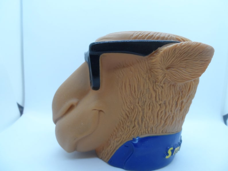 May include: A brown camel head figurine wearing black sunglasses and a blue and yellow collar with the word "Smokin'" on it.