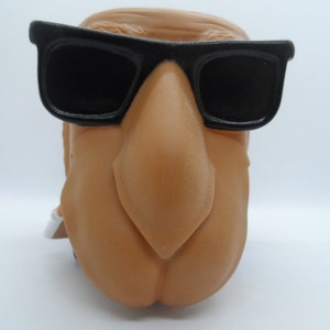 May include: A brown camel figurine wearing black sunglasses. The camel has a large, prominent nose.