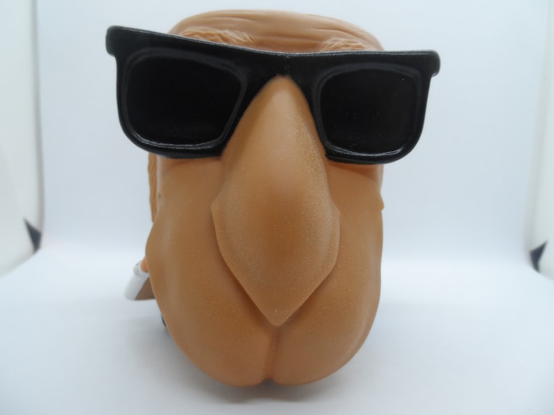 May include: A brown camel figurine wearing black sunglasses. The camel has a large, prominent nose.