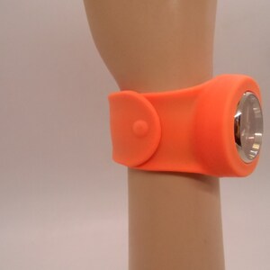 May include: Orange silicone wristwatch with a silver face and a buckle closure.