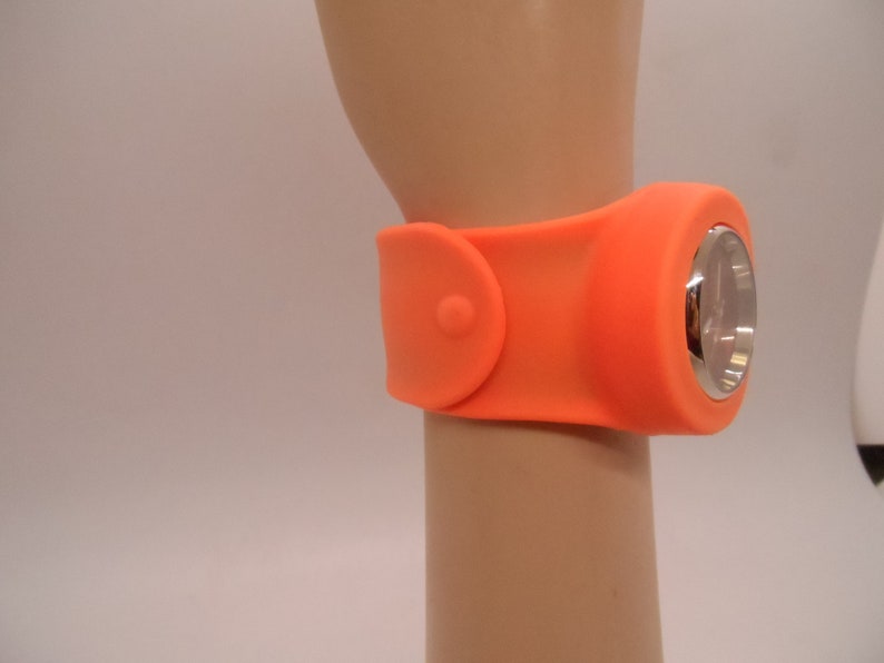 May include: Orange silicone wristwatch with a silver face and a buckle closure.