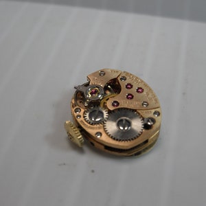 May include: Close-up of a gold-toned watch movement with visible gears and ruby jewels. The movement is labeled "Swiss Made" and "17 Jewels".