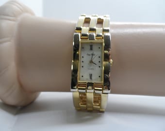 May include: A gold-tone watch with a white face and Roman numeral hour markers. The watch has a gold-tone metal band with a rectangular shape.