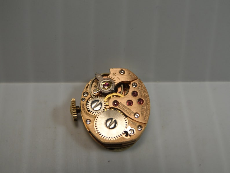 May include: Close-up of a gold-toned watch movement with intricate gears and a red jewel. The movement is labeled "Eterna-Matic" and "Swiss Made".