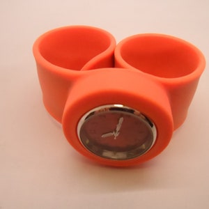 May include: Orange silicone wristwatch with a silver face and white hands.