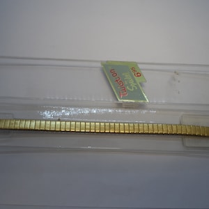 May include: A gold-toned watch band in a clear plastic package. The package has a label that reads "Tusscon Sparkle 9.65".