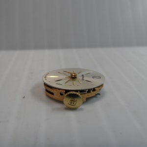 May include: A close-up of a silver watch face with gold hands and a gold winding stem. The watch face has the word "SEIKO" printed on it.