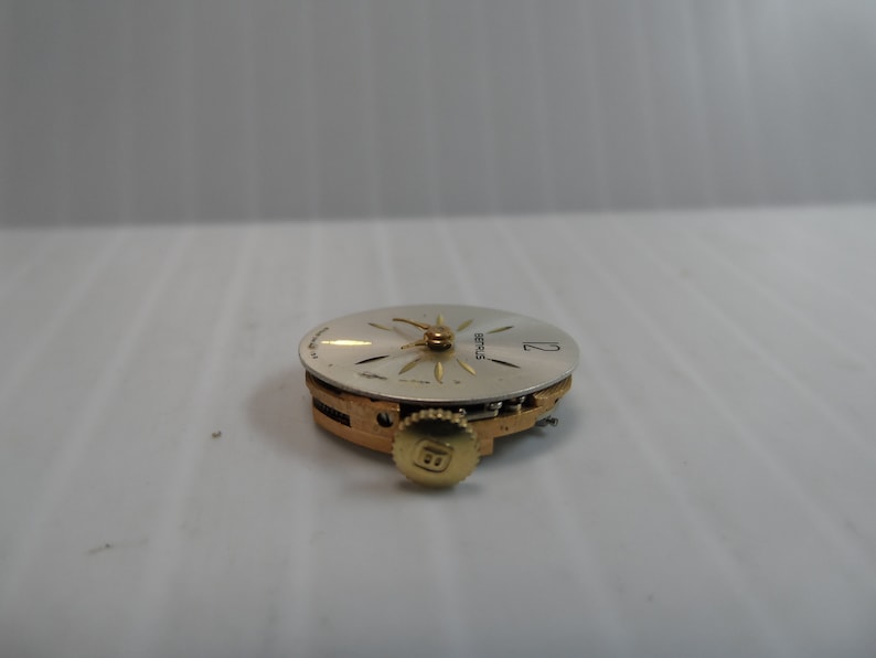 May include: A close-up of a silver watch face with gold hands and a gold winding stem. The watch face has the word "SEIKO" printed on it.