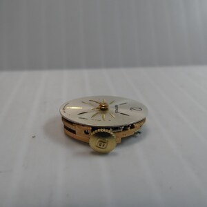May include: A close-up of a silver watch face with gold hands and a gold winding stem. The watch face has the word "SEIKO" printed on it.