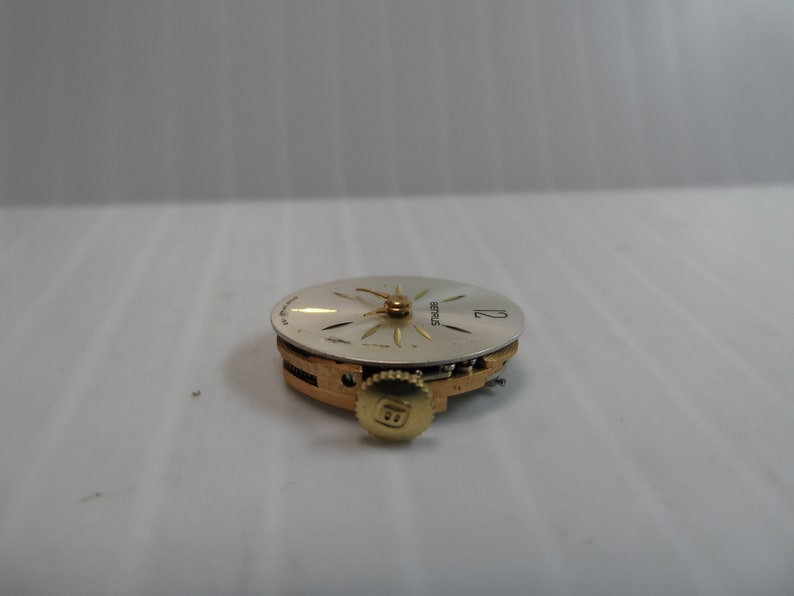May include: A close-up of a silver watch face with gold hands and a gold winding stem. The watch face has the word "SEIKO" printed on it.