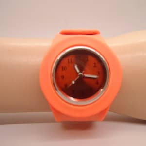 May include: A bright orange silicone wristwatch with a round face and black numbers. The watch has a silver rim around the face and a black second hand.