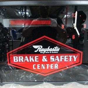 Puede incluir: Señal iluminada negra y roja con un reloj y el texto "Raybestos The best in brakes Brake & Safety Center".