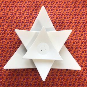 May include: A set of three white ceramic triangular dishes stacked on top of each other. The dishes are in the shape of a star.