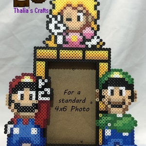 May include: A pixel art picture frame featuring Mario, Luigi, and Princess Peach. The frame is made of colorful plastic beads and is designed to hold a standard 4x6 photo.