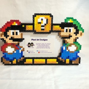 Op de afbeelding: Een pixel art fotolijst met Mario en Luigi uit de Super Mario Bros. videogame. De lijst is gemaakt van kleurrijke perler kralen en is een geweldige manier om foto's of kunstwerken te tonen.