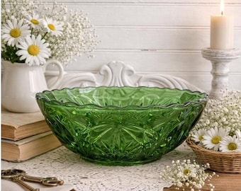 May include: A large, green glass bowl with a scalloped rim. The bowl has a starburst pattern and sits on a lace doily. Daisies and baby's breath are in a white pitcher and a small basket. A lit candle is in the background.