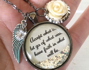 May include: A silver necklace with a round pendant that says "Accept what is, let go of what was, have faith in what will be." The pendant is filled with glitter and has a white rose charm attached to it.