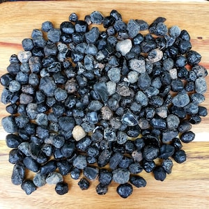 May include: A close-up of a large pile of black obsidian stones. The stones are smooth and polished, and they have a dark, almost black color. The stones are arranged in a random pattern, and they are all about the same size.