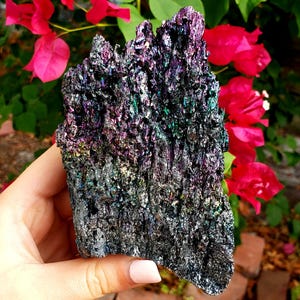 May include: A large, iridescent black crystal with a rough, textured surface. The crystal has a purple, green, and blue sheen.