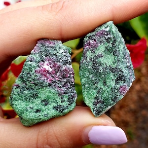 May include: Two pieces of green and pink zoisite rough, a type of gemstone, with a rough, irregular shape.