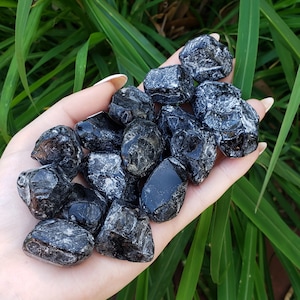 May include: A collection of black obsidian tumbled stones with a silvery sheen. The stones are smooth and polished, and they are held in a hand.