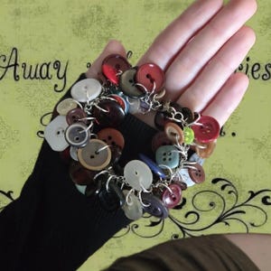 May include: A handmade button bracelet featuring a variety of colorful buttons in shades of red, brown, white, and blue. The buttons are connected with silver-colored chain links, creating a unique and eclectic accessory.