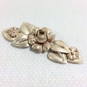 May include: Silver brooch with a floral design. The brooch features a central rose with leaves and smaller flowers.