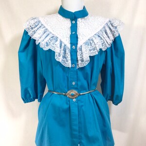 May include: A turquoise blue button-up shirt with a white lace collar and a silver belt with a turquoise stone buckle.