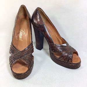 May include: A pair of brown snakeskin platform heels with a peep toe and criss-cross straps. The heels are about 4 inches tall and the platform is about 1 inch tall. The shoes are labeled "Ferrant" on the insole.