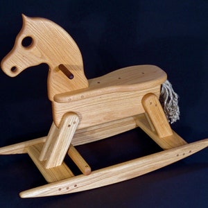 May include: A wooden rocking horse toy with a natural wood finish. The horse has a carved head with large eyes and a tail made of rope. The rocking base is made of wood and has a smooth finish.