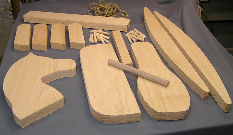 May include: A set of wooden pieces for building a rocking horse. The pieces are made of light-colored wood and include the head, body, legs, and rockers. There are also dowels and rope included in the set.