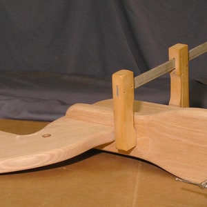 May include: A wooden rocking horse is being clamped together with two wooden clamps and a metal bar. The horse is made of light wood and has a smooth finish.