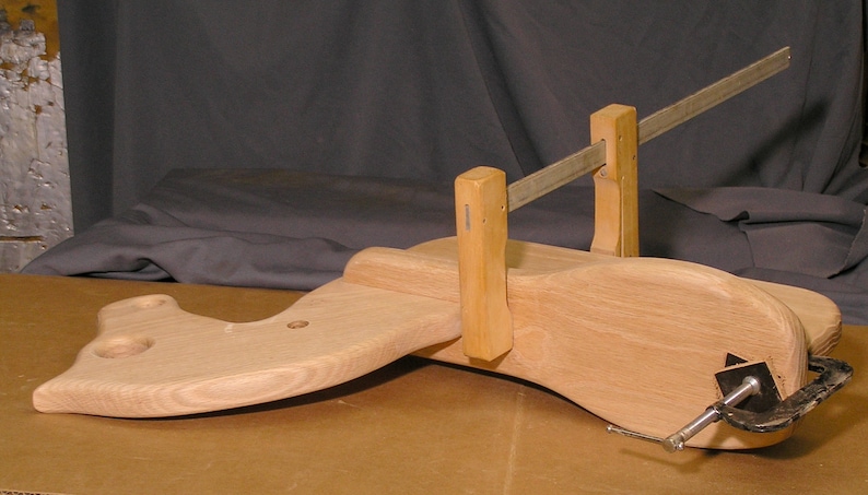 May include: A wooden rocking horse is being clamped together with two wooden clamps and a metal bar. The horse is made of light wood and has a smooth finish.