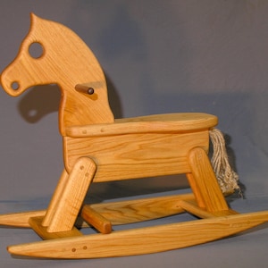 May include: A wooden rocking horse with a natural wood finish. The horse has a rope tail and a wooden saddle. The rocking base is made of wood and has a natural wood finish.