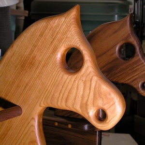 May include: Two wooden rocking horses, one light brown and one dark brown, with carved details and holes for the rider's hands and feet.