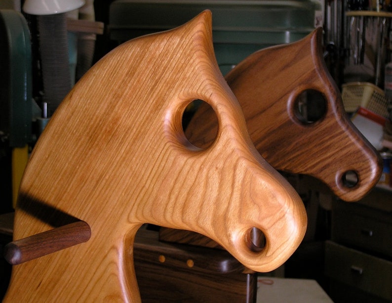 May include: Two wooden rocking horses, one light brown and one dark brown, with carved details and holes for the rider's hands and feet.