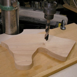May include: A drill bit is being used to drill holes in a piece of wood. The wood is shaped like a horse's head and is being held in place by a clamp.
