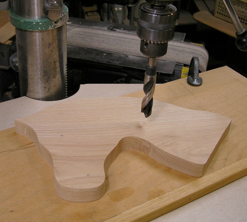 May include: A drill bit is being used to drill holes in a piece of wood. The wood is shaped like a horse's head and is being held in place by a clamp.