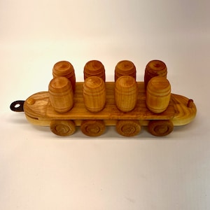 May include: A wooden toy train carrying eight wooden barrels. The train has six wheels and is made of light brown wood.