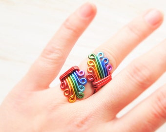 Puede incluir: Dos anillos de alambre de arcoíris con una base roja. Los anillos están hechos de alambre de colores que se tuerce y se da forma a un diseño que se asemeja a un abanico o una pluma de pavo real.