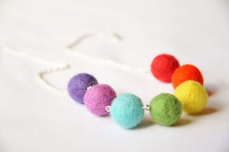 Puede incluir: Un collar colorido hecho de bolas de fieltro en tonos de morado, rosa, turquesa, verde, amarillo y rojo. El collar est&aacute; enhebrado en una cadena plateada.