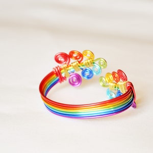 May include: A rainbow-coloured wire bracelet with a decorative swirl design. The bracelet is made of multiple strands of wire, each a different colour of the rainbow.