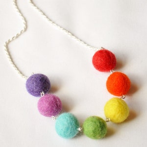 Puede incluir: Un collar de bolas de fieltro de colores arco&iacute;ris con una cadena plateada. Las bolas est&aacute;n en el orden de rojo, naranja, amarillo, verde, azul y morado.